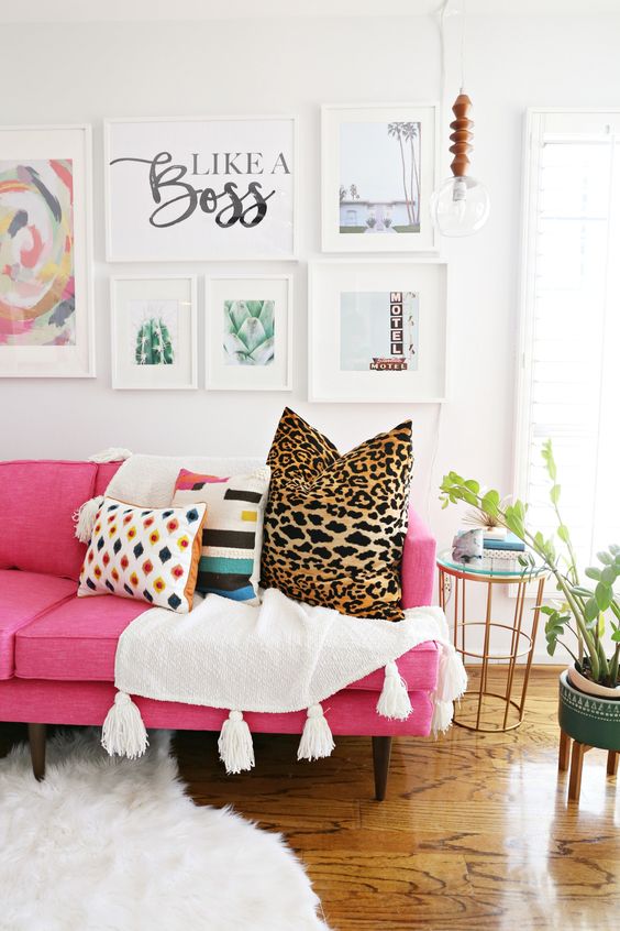 a modern living room with a hot pink sofa, printed pillows, a chic gallery wall, a pendant bulb and potted plants