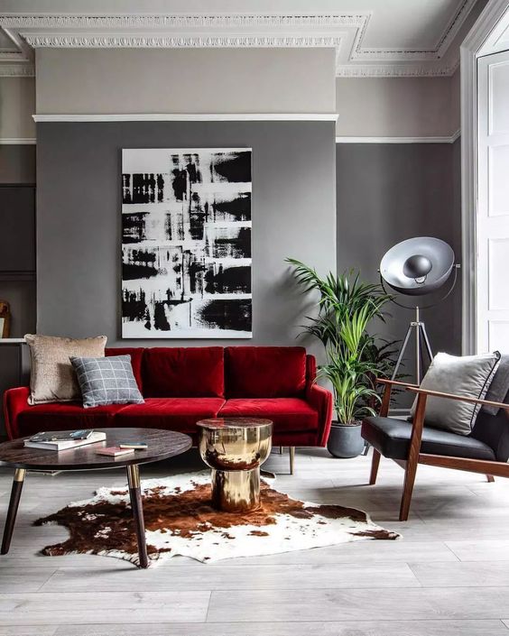 a modern living room with grey walls, a bold red sofa, a black leather chair, a monochromatic artwork and a round table