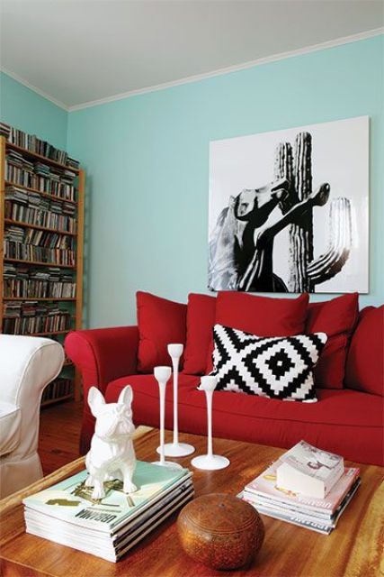 a modern living room with turquoise walls, a bold red sofa, a bookcase, a monochromatic artwork and a low table with decor