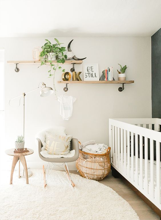 a modern neutral nursery with a grey accent wall, a large white crib, a grey chair, a basket and some wooden shelves