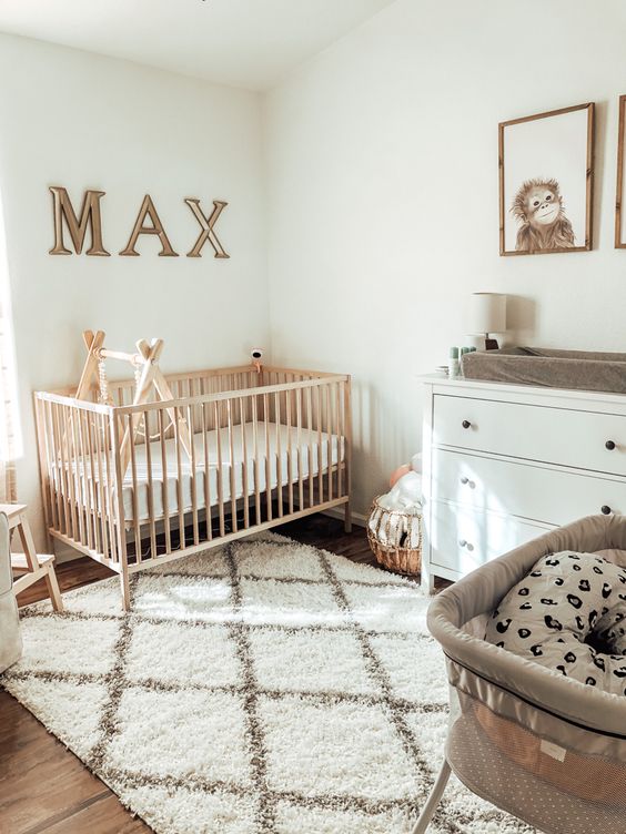 a modern neutral nursery with a stained crib, a white dresser, a printed rug, a letter art and some other artworks