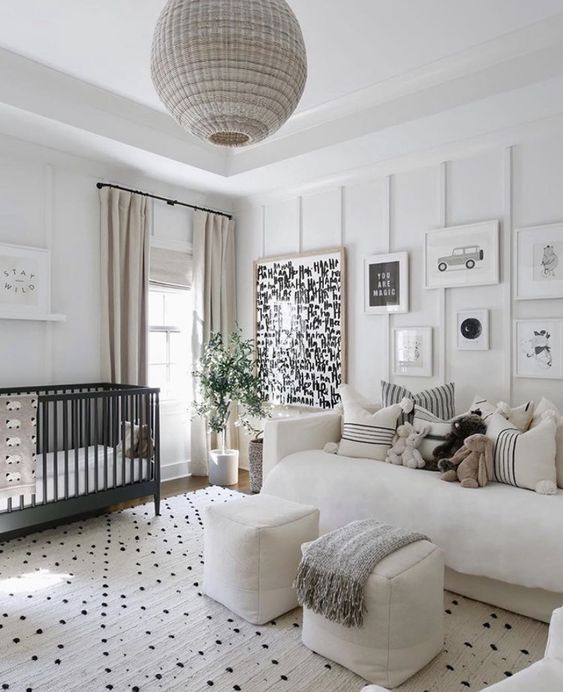 a modern neutral nursery with paneled walls, a black crib, neutral furniture, a gallery wall, printed textiles and a rattan pendant lamp