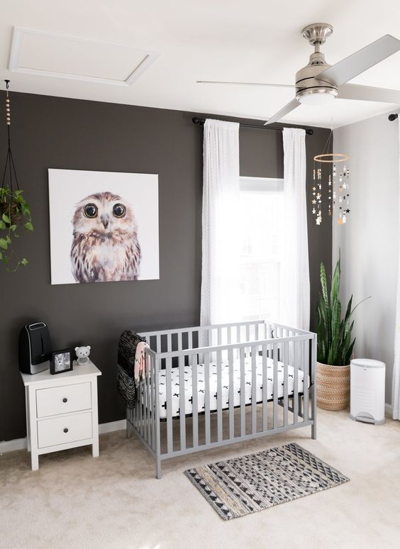 a modern nursery with a black accent wall, a grey crib, potted plants, a printed rug and neutral curtains is very cool