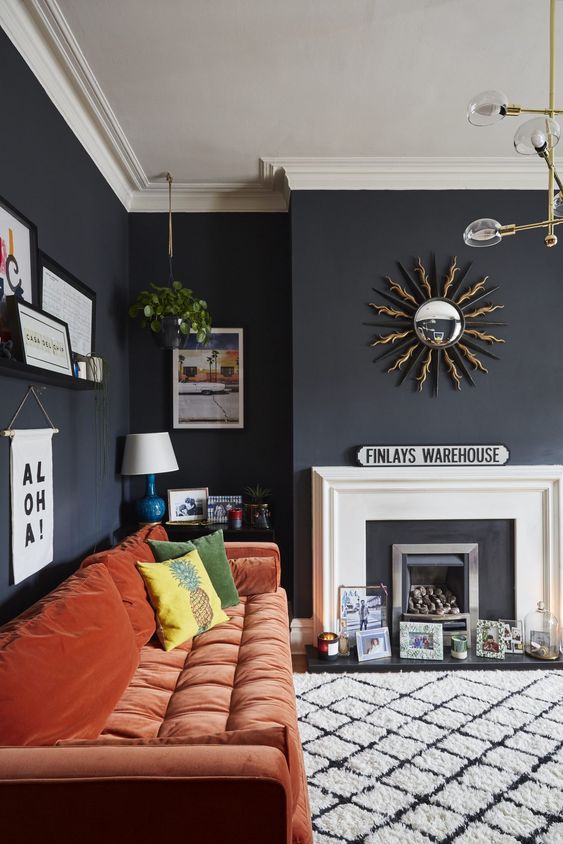 A moody living room with a faux fireplace, artworks, prints and candles, a rust colored sofa and a pretty gallery wall