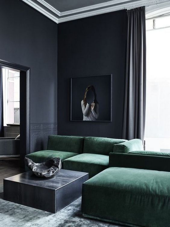 a moody living room with black walls, a low emerald sofa, a low metal coffee table and a statement artwork