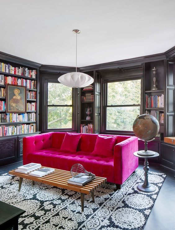 A moody room with a bay window, built in bookshelves, a hot pink tufted sofa for a color accent in the space