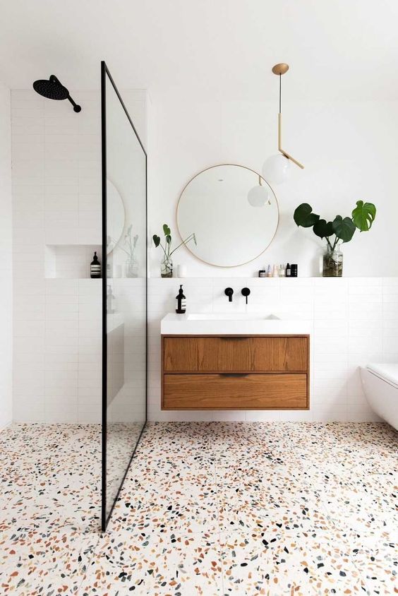 A neutral mid century modern bathroom done in neutrals, with white skinny tiles, a terrazzo floor and with black and brass fixtures and touches
