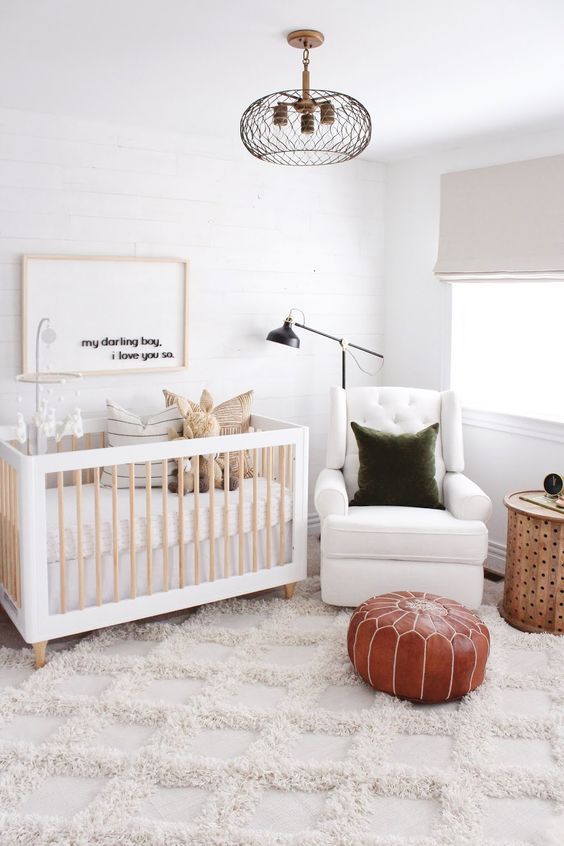 a neutral nursery with a cool crib, a white chair, a green pillow and a brown leather pouf plus pillows and toys