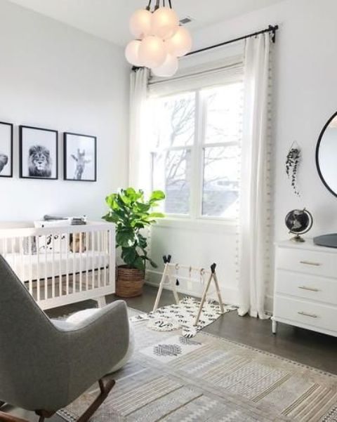 a neutral nursery with a white crib, a grey rocker, a white dresser, a statement plant and a gallery wall with black and white art