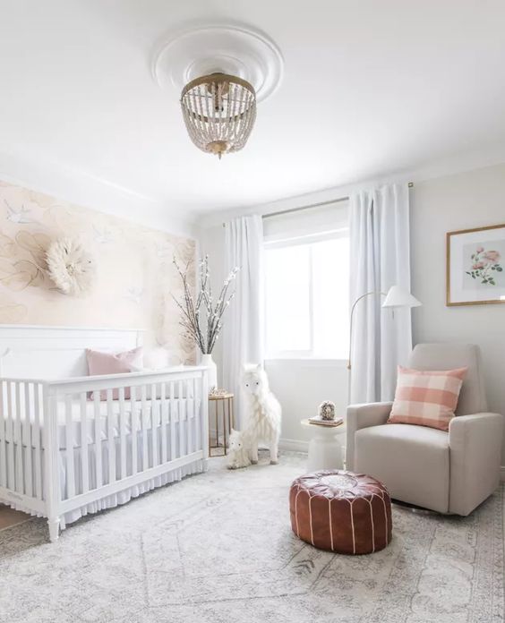 a neutral nursery with neutral furniture, a leather pouf, a beaded chandelier and printed pillows
