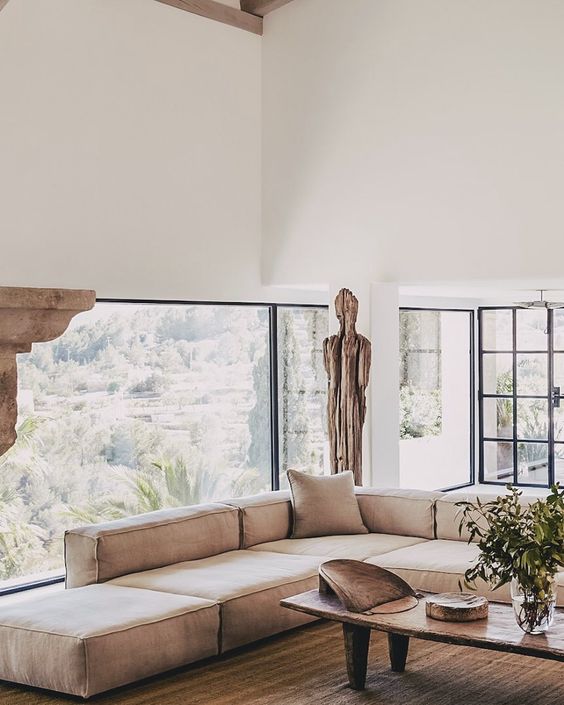 a neutral serene living room with a glazed wall, a low tan sofa, touches of wood, a wabi-sabi low coffee table and greenery