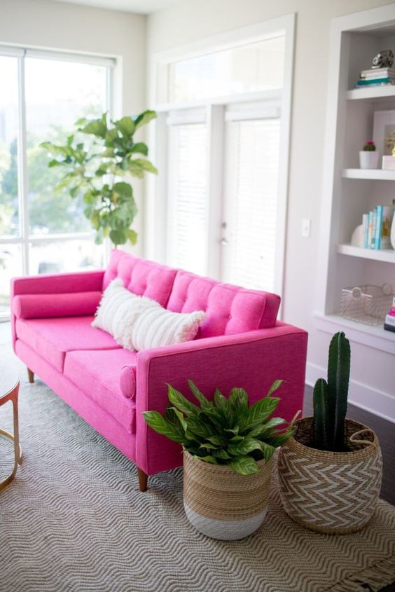 a neutral space spruced up with a hot pink sofa, a boho rug and pillows, potted plants in baskets is a cool room