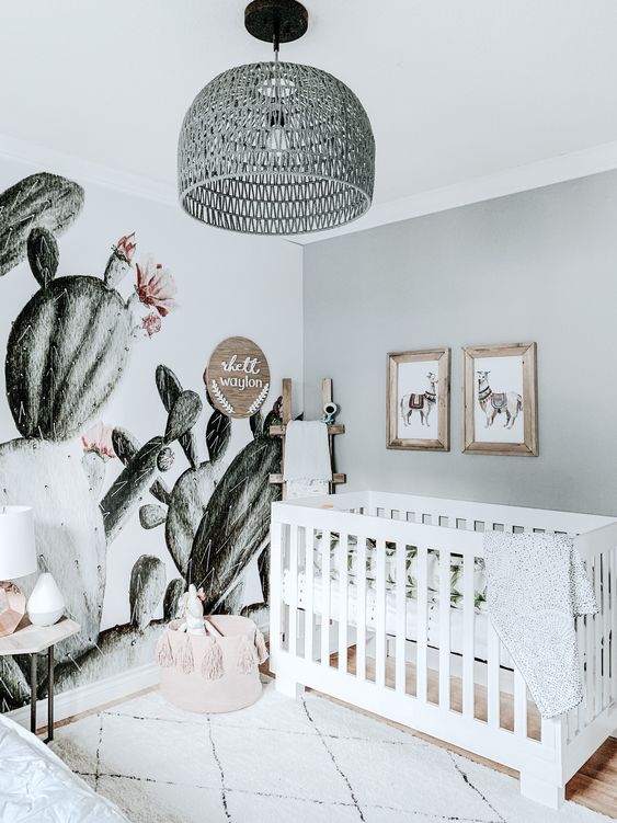 a playful neutral nursery with a grey wall, a white crib, a printed rug and a gorgeous cactus wall mural plus a pendant lamp