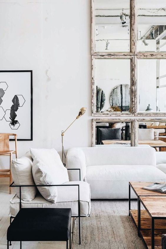 a pretty living room with a white low sofa, a low wooden table, a black stool, a mirror framed wall and a cool artwork