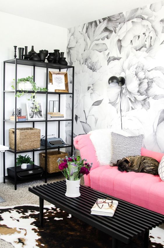 a pretty monochromatic living room with a floral wall, a storage unit, a black table and a bright pink sofa with printed pillows
