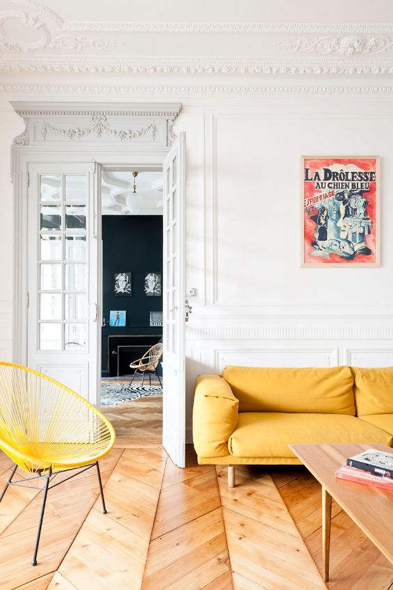 a refined Parisian living room with a yellow sofa and achair, a low table and a vintage poster on the wall