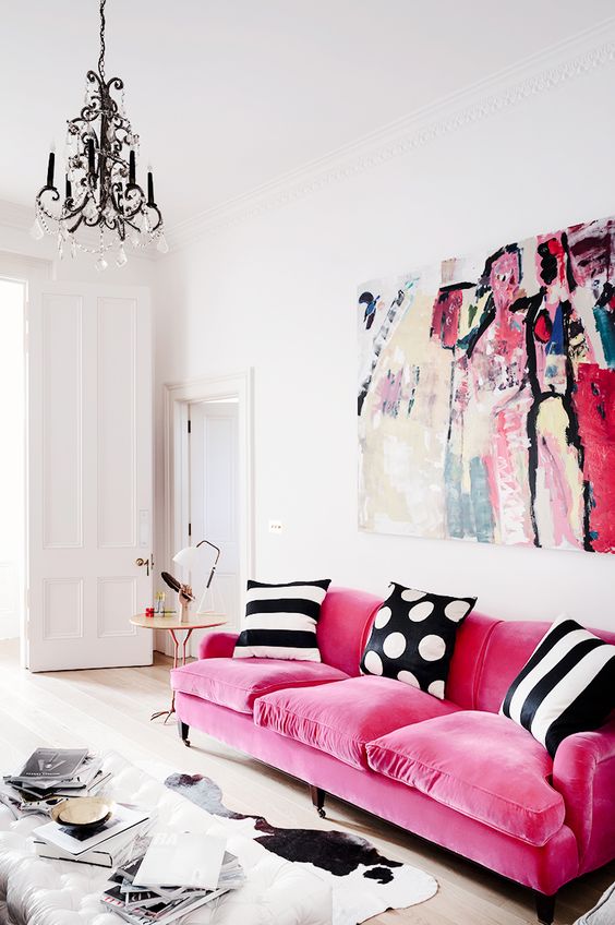 a refined contemporary living room with a hot pink sofa with printed pillows, a bold artwork, a crystal chandelier and a white ottoman