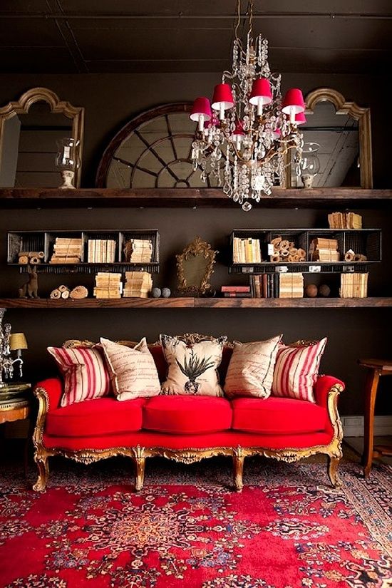 a refined eclectic living room with dark walls, dark stained shelves, a refined gold and red sofa and a catchy chandelier