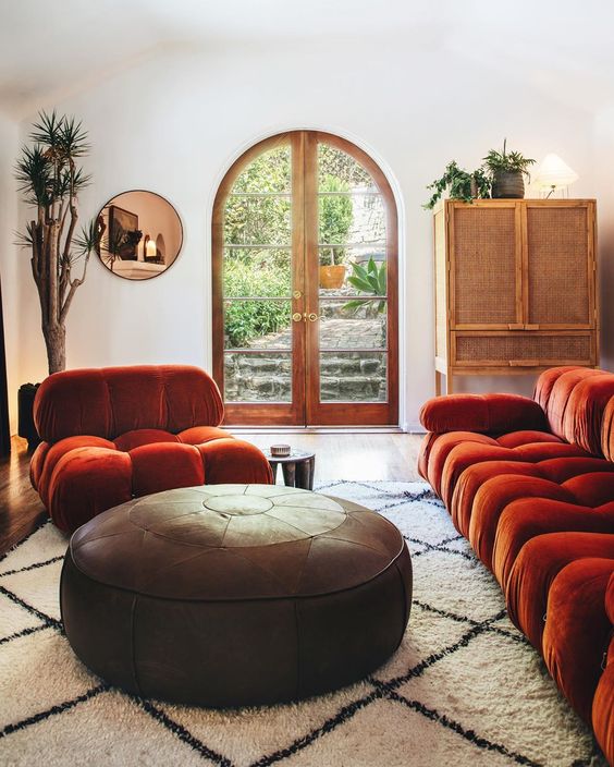a refined living room in neutrals, with a burnt orange sofa and a chair, a round leather ottoman, a rattan sideboard