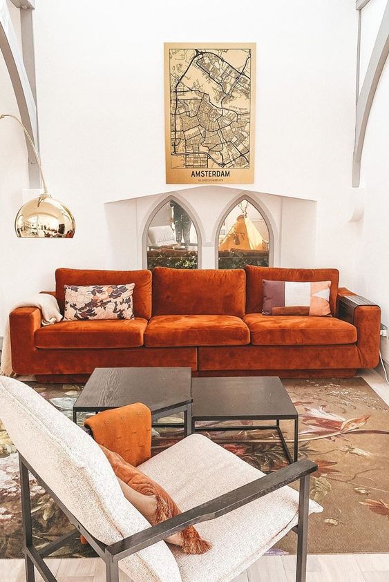 a refined living room with a rust-colored sofa, a duo of tables, a creamy chair, a polished floor lamp is amazing