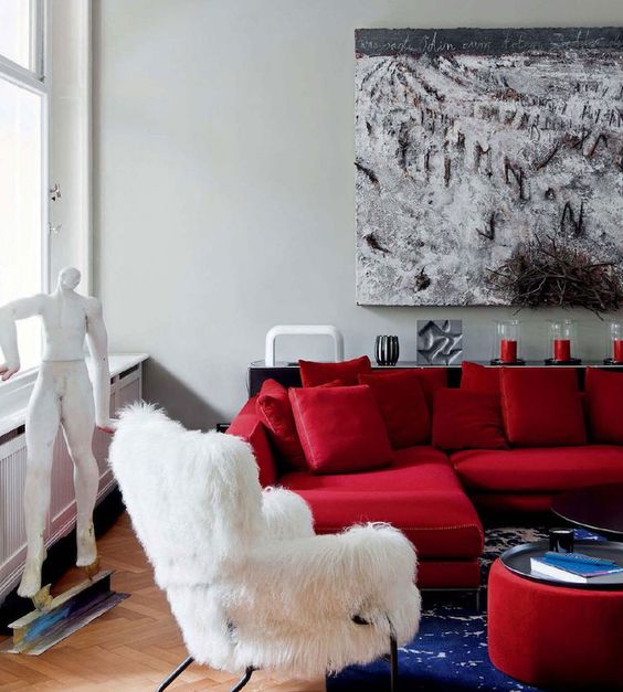 a refined modern living room with a hot red sectional, a white faux fur chair, a bold red ottoman and a creative artwork