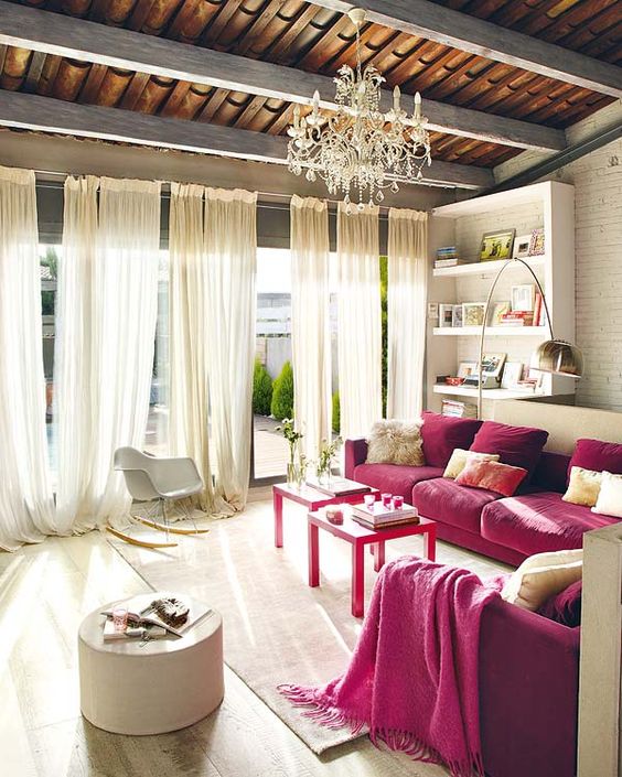 A refined neutral living room with built in shelves, two fuchsia sofas, neutral furniture and textiles plus a crystal chandelier