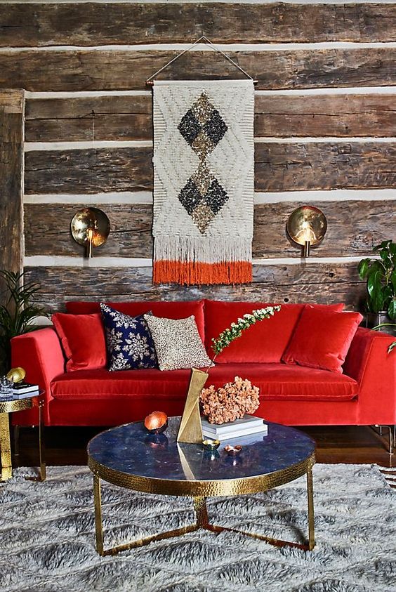 a rustic living room with wood wallpaper walls, a bold red sofa, a refined blue marble table and touches of gold here and there