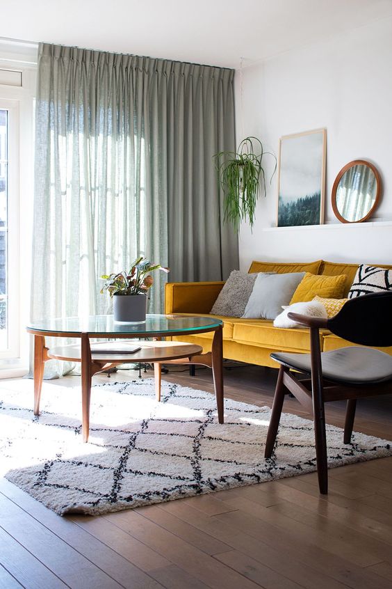 a simple and cool mid-century modern living room with a yellow sofa, graphic pillows, a modern chair and table plus green curtains