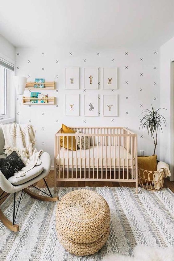 a simple modern nursery with an accent wall, a light stained crib, a grey rocker, a rattan basket and some shelves for books