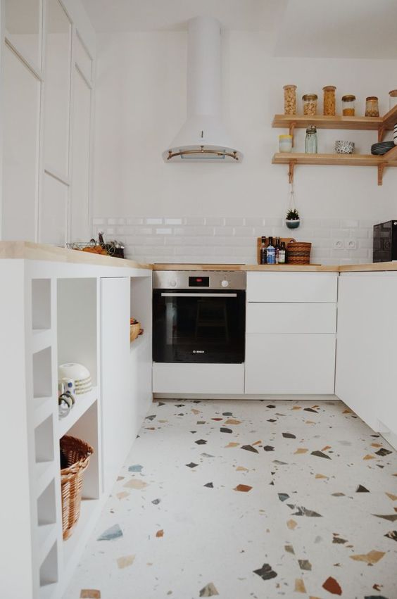 a small neutral kitchen with sleek cabinets and butcherblock countertops, a white hood and a fun terrazzo floor that brings a playful feel here