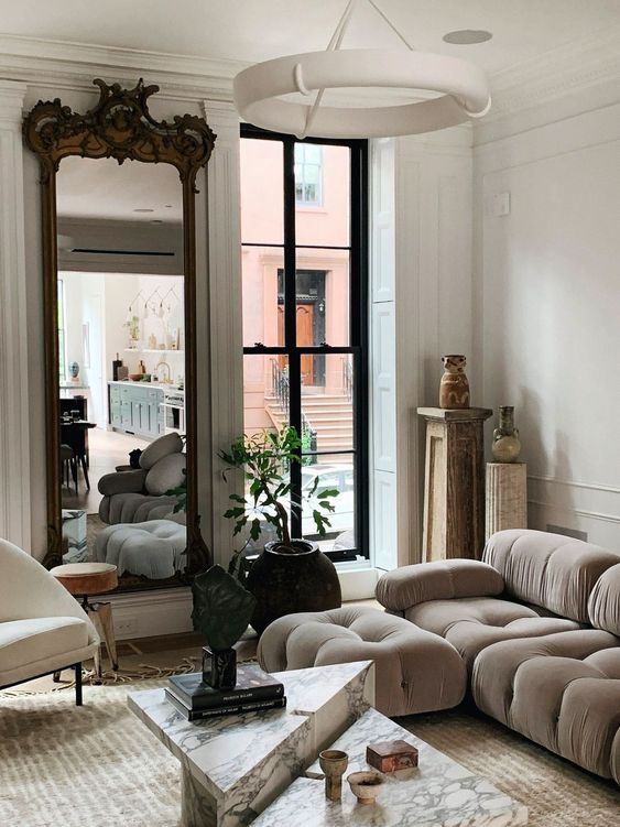 a sophisticated living room with a grey low sofa, marble tables, a large mirror in a refined frame and a potted plant