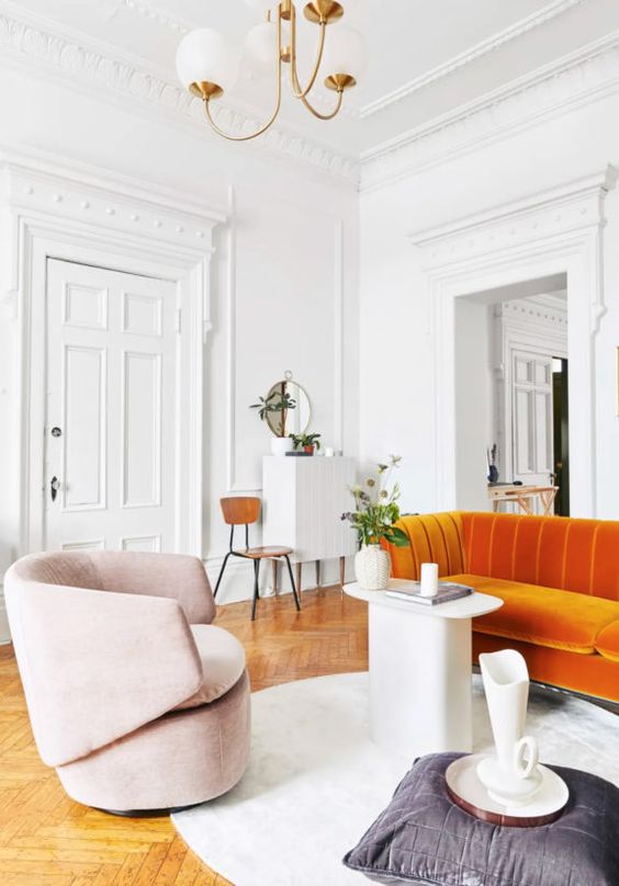 a sophisticated living room with an orange sofa, a pink chair, a quirky table and a pillow plus a jug is a catchy space