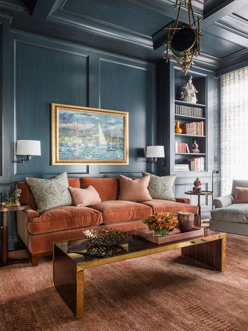 A sophisticated living room with navy walls, a rust colored velvet sofa, a low polished table, built in shelves