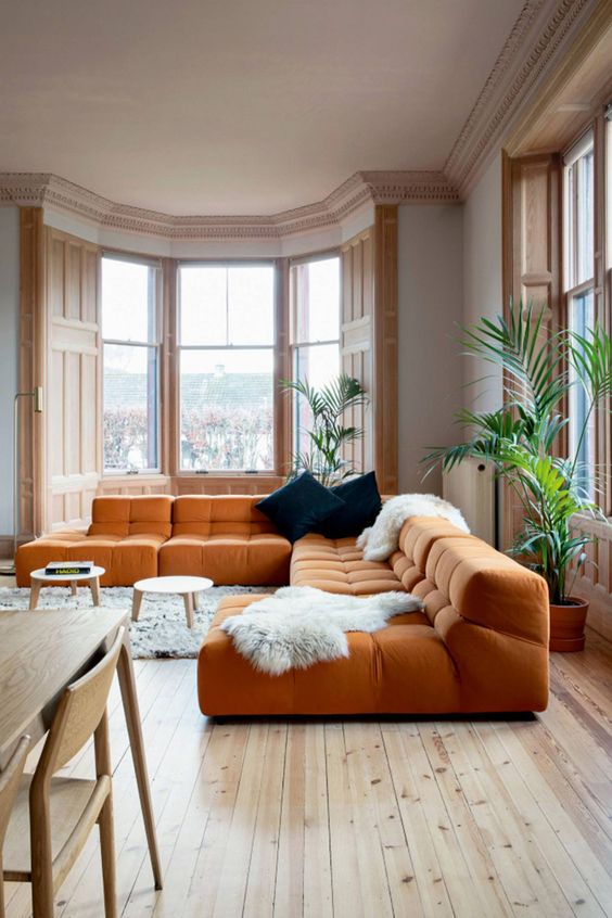 a spacious living room with a low orange sofa, faux fur, navy pillows and gorgeous light stained windows