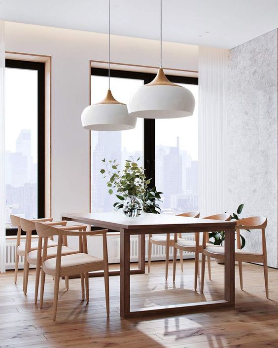 A stylish mid century modern dining room with a dining table and blonde wood chairs with neutral seats plus elegant pendant lamps