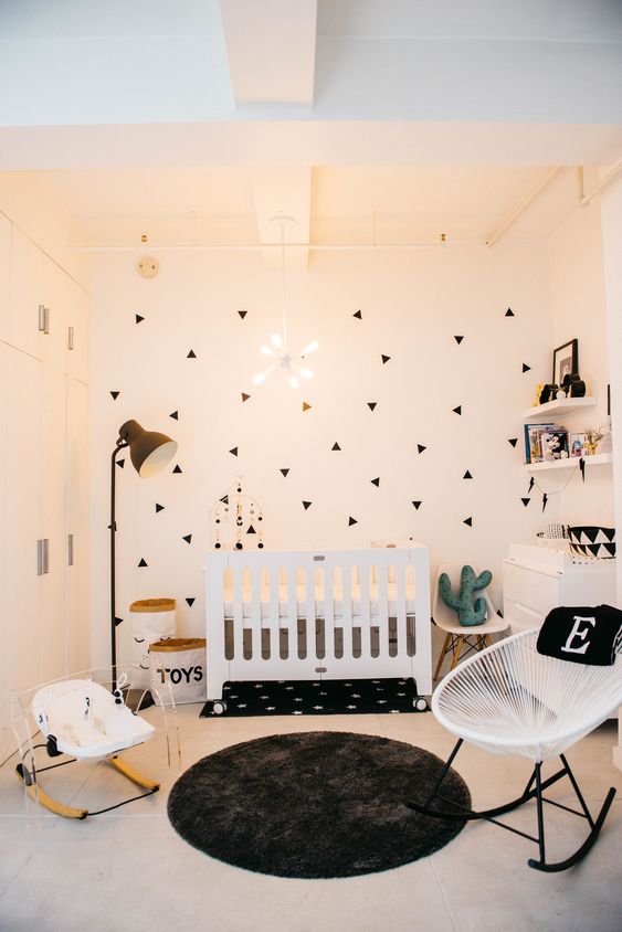 a stylish modern nursery with a geo print wall, white furniture, a floor lamp, floating shelves and a cool modenr chandelier