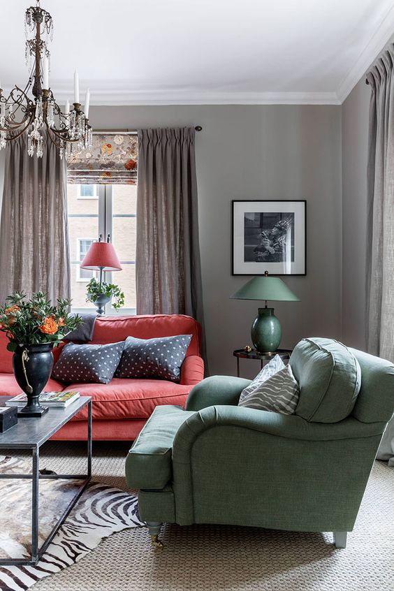 a vintage Scandi-inspired interior with grey walls, a red sofa, a green chair and a vintage crystal chandelier