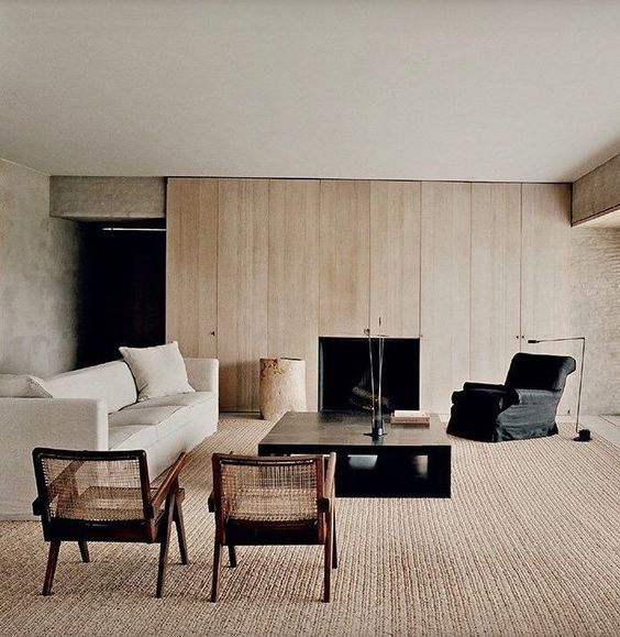 a warm neutral contemporary living room with a blonde wood wall, a fireplace, chic furniture and a large carpet