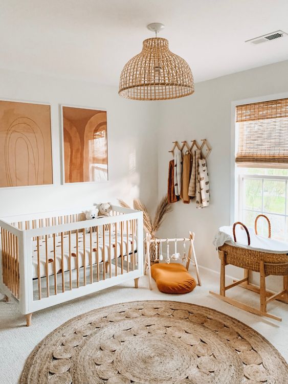 a warm neutral nursery with a cool crib, a baby cot, a jute rug, some artworks, shutters and a rattan lamp over the space