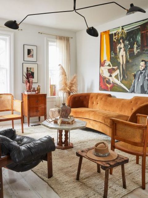 A welcoming 70s inspired living room with a rust colored sofa, rattan, wooden and leather furniture, a black chandelier and a statement artwork
