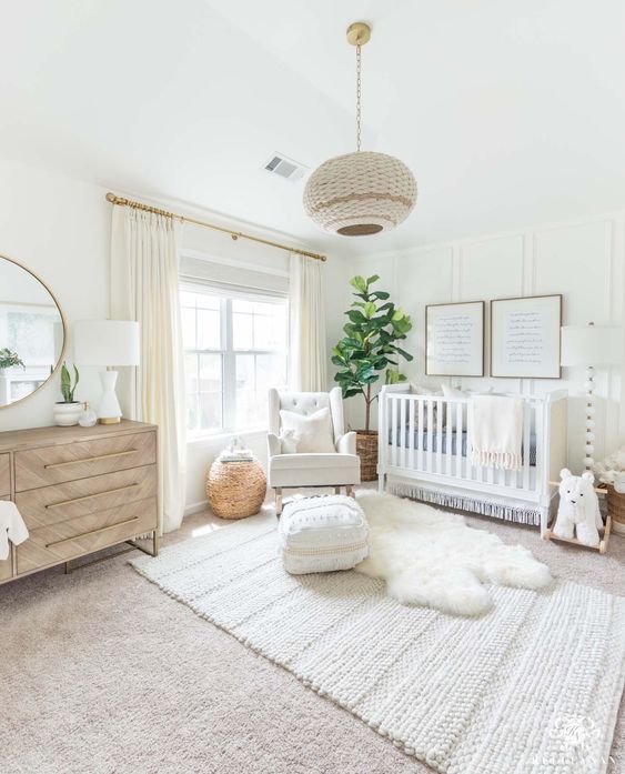 a welcoming neutral nursery with a cool crib, a light stained dresser, layered rugs, a pendant lamp, a graphic gallery wall and a statement potted plant
