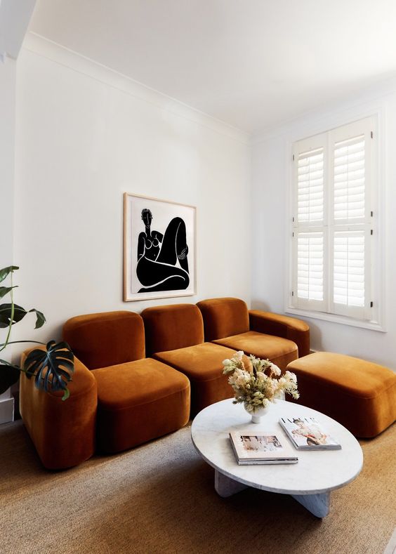 a whimsical living room with a quirky rust-colored sofa and an ottoman, a round table and a bold artwork