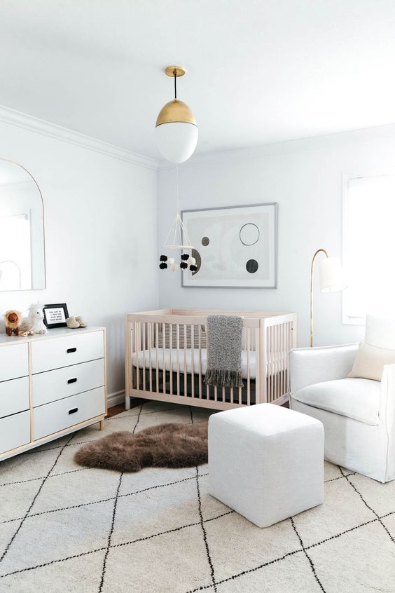 an airy modern nursery with white walls, white furniture and a light-stained crib, layered rugs and abstract decor