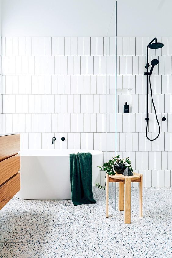 an airy neutral bathroom with white skinny tiles, a white terrazzo floor, a floating wooden vanity and a wooden stool