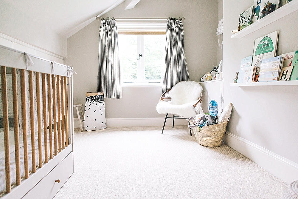 an airy neutral nursery with a grey crib, floating shelves, a rattan chair and a dresser plus striped curtains