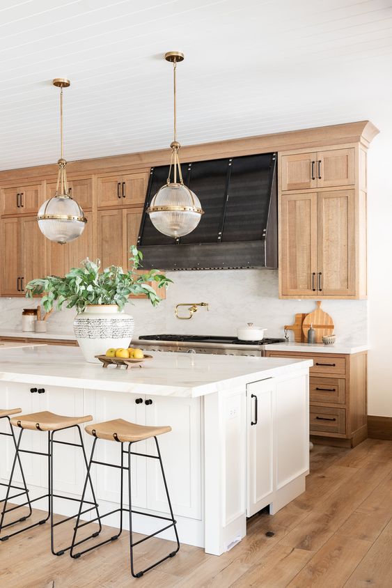 an amazing modern farmhouse kitchen with blonde wood cabinets, a white kitchen island, pendant lamps and blonde wood stools
