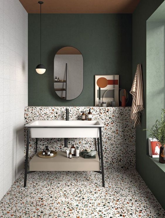 an eye-catchy bathroom with a dark green accent wall, catchy terrazzo tiles on the floor and wall and a cool free-standing sink