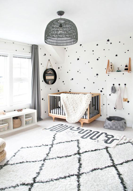 an ultra-modern monochromatic girl's nursery with a black star print wall, a chic crib, a storage bench, a shelf and a grey rattan chandelier