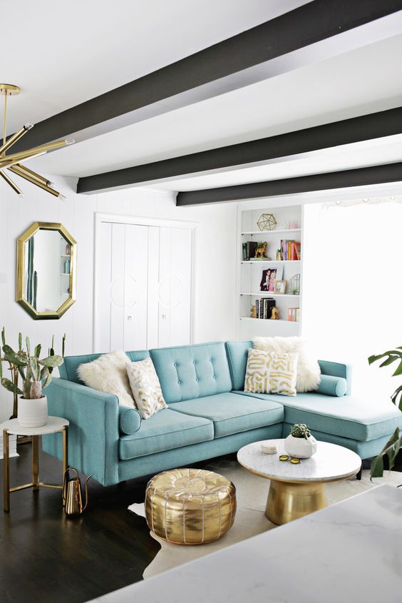 A beautiful mid century modern living room with a fireplace, dark beams on the ceiling, a turquoise sofa and touches of gold for more elegance