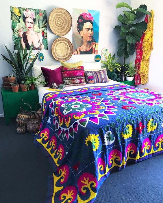 a boho maximalist bedroom with a navy carpet on the floor, emerald nightstands, a bold gallery wall, potted plants and bright textiles